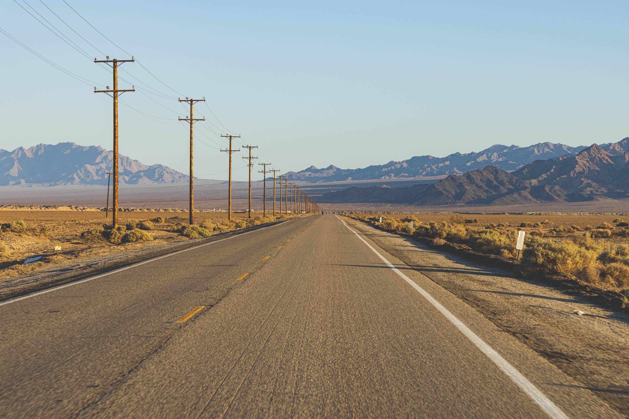 A road and power lines run off into the mountainous distance