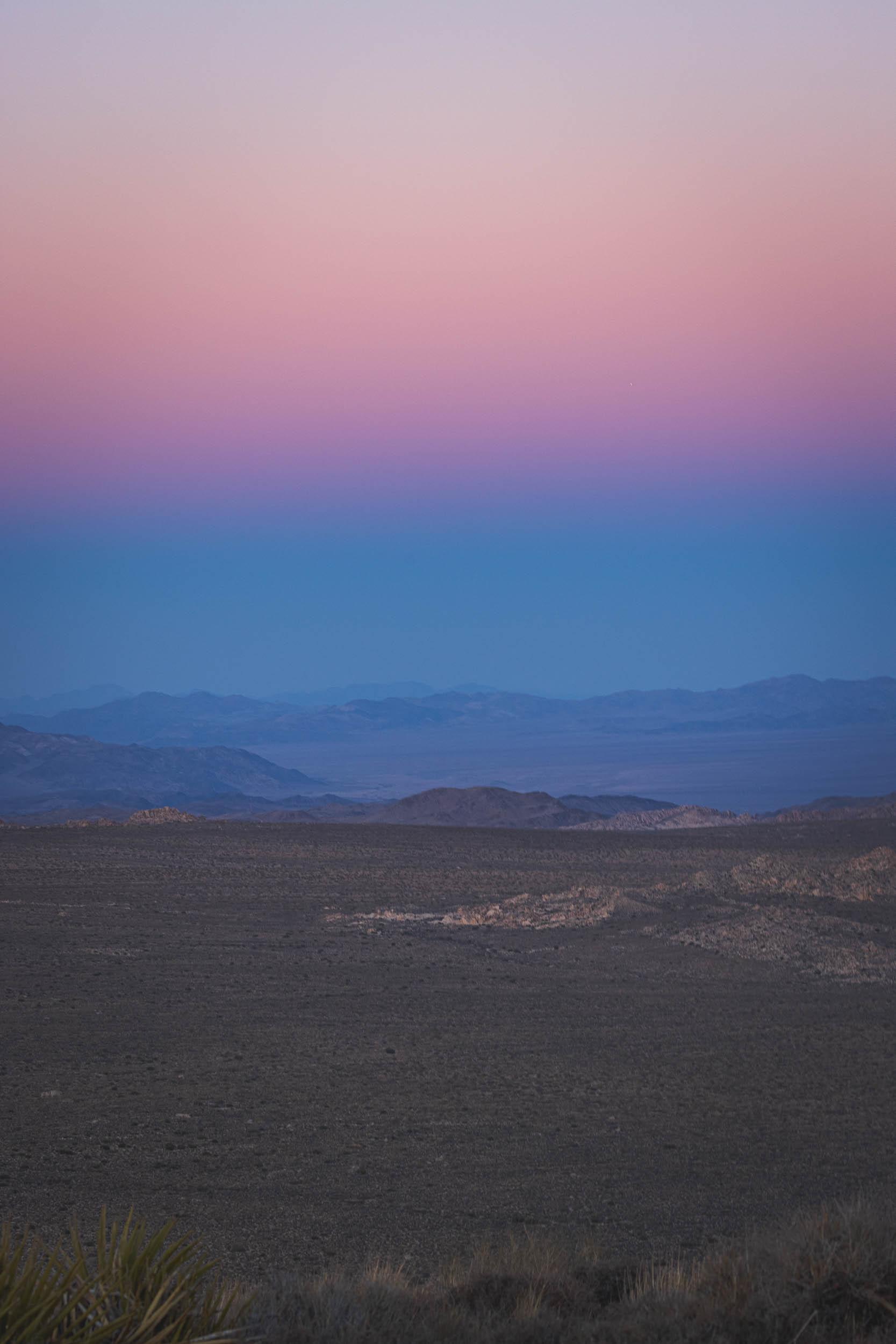 The shadow of the sunset as the sun dips below mountains in the distance