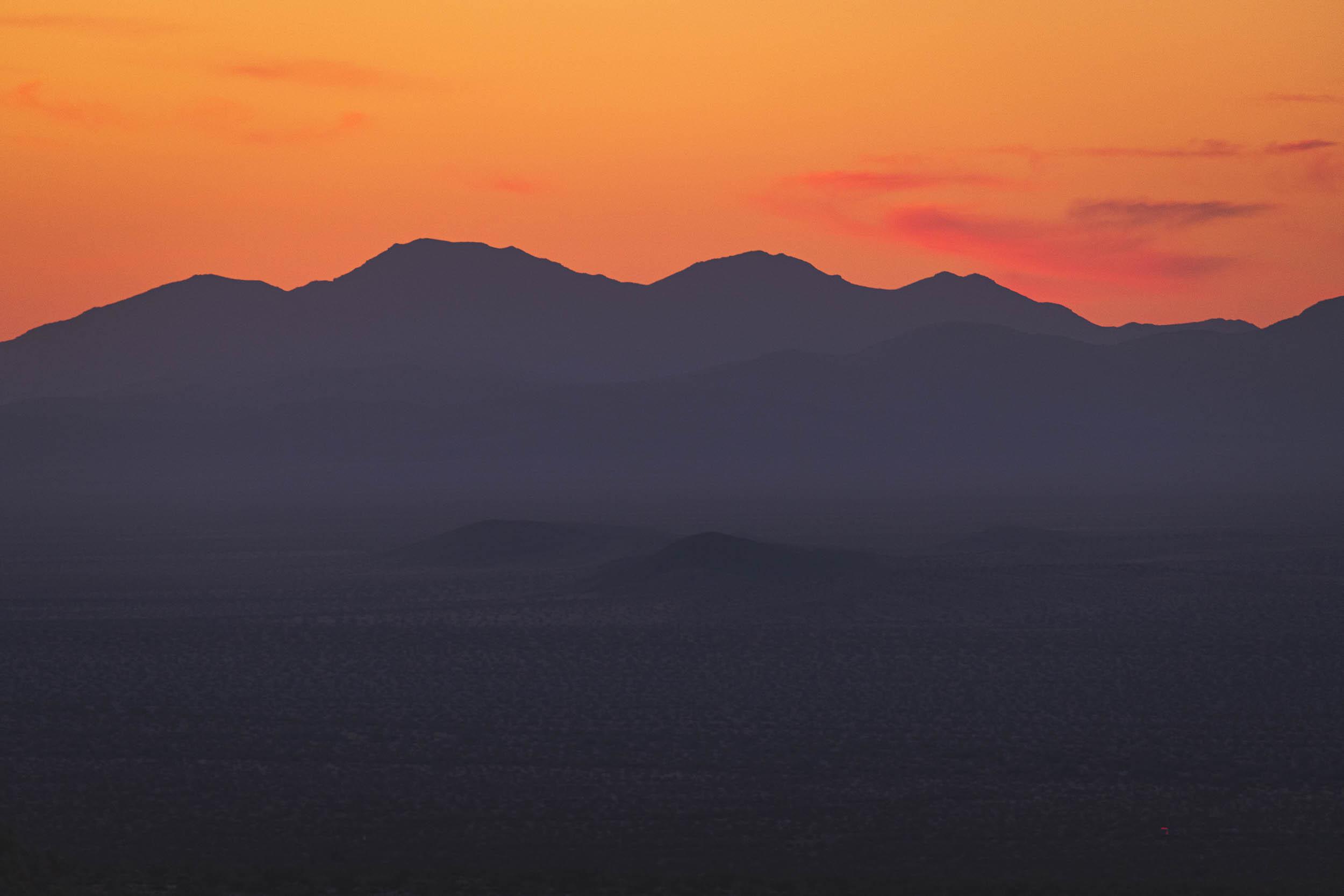 The shadow of the sunset as the sun dips below mountains in the distance