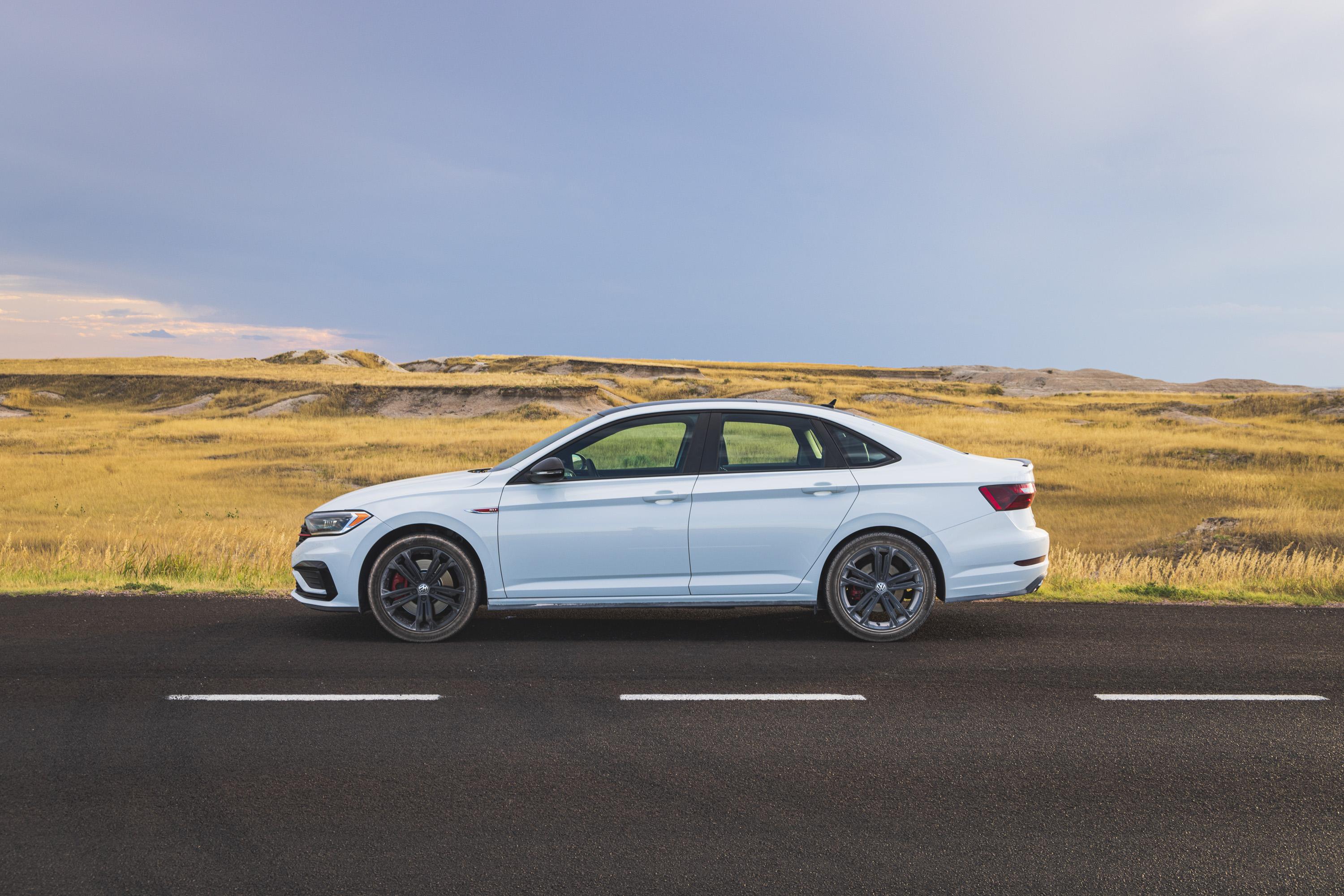A profile view of my white Volkswagen, covered in a light dust, sits at the side of the road with grassland stretching out behind it