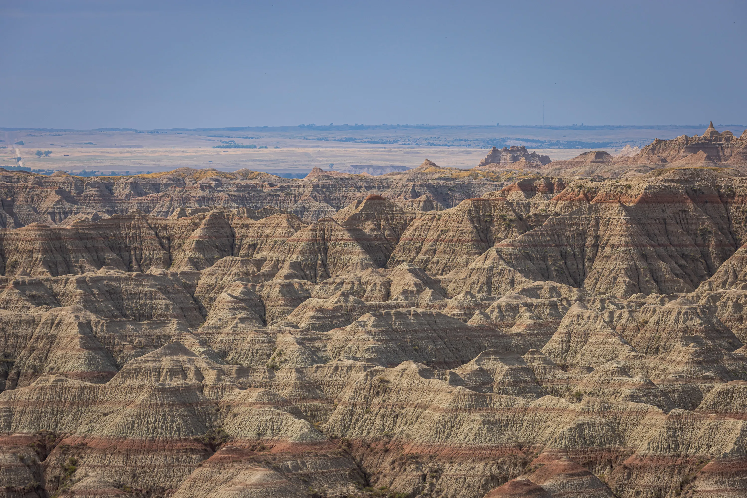 A mile or two of peaks rounded by time, split by clear layers in the material stretch away in the foreground, behind which you can see flat grassland