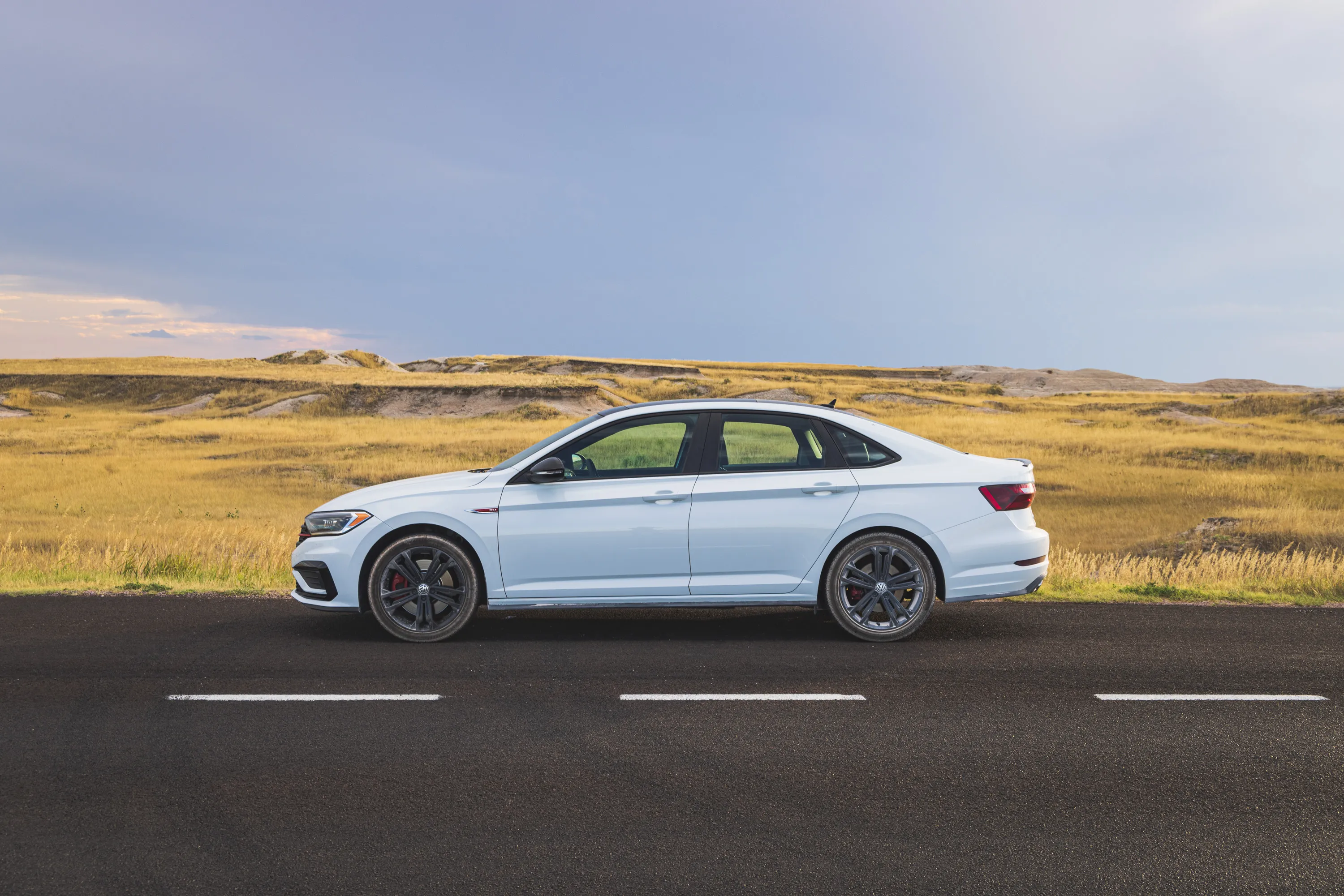 A profile view of my white Volkswagen, covered in a light dust, sits at the side of the road with grassland stretching out behind it