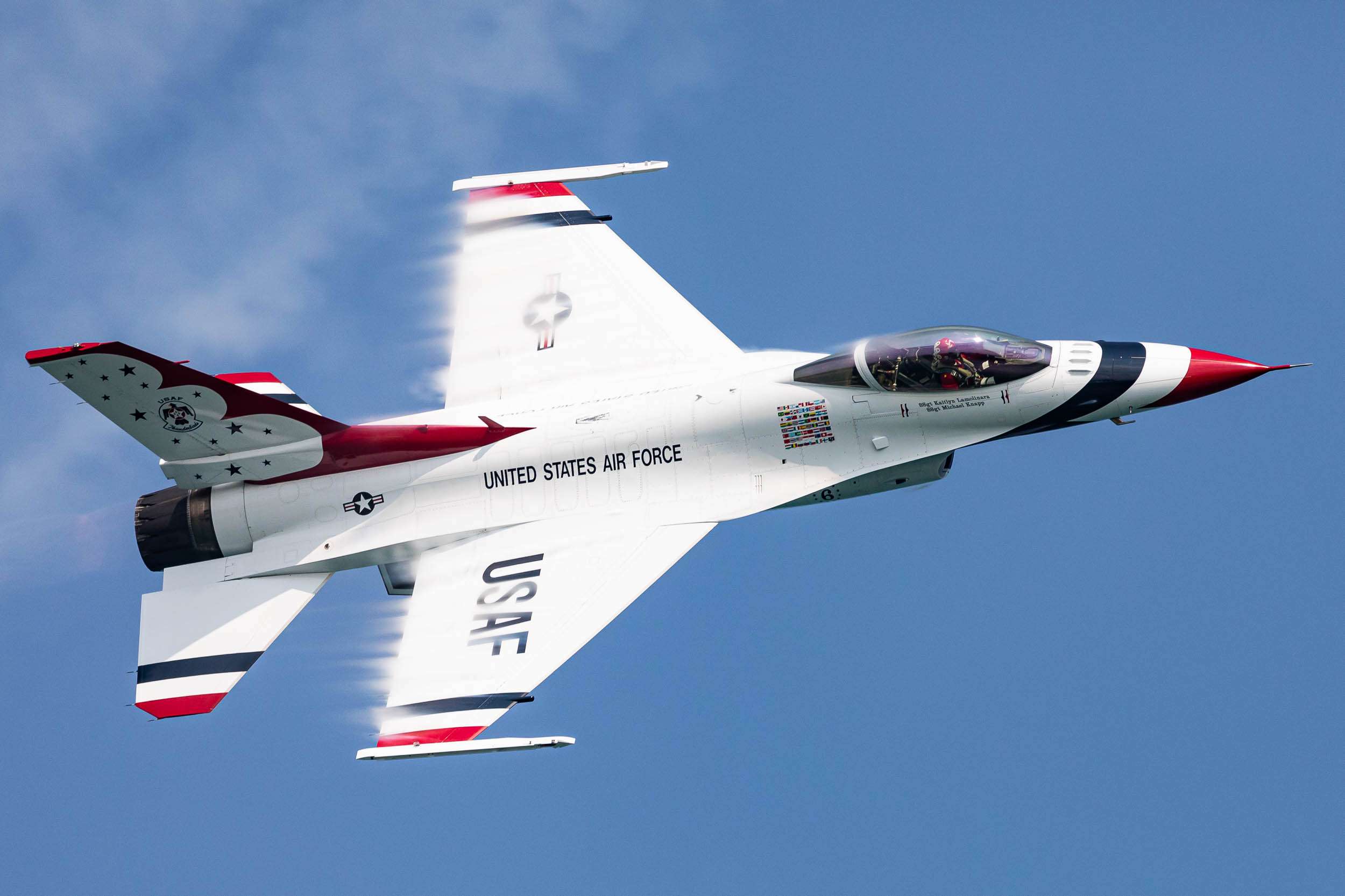 A US Air Force Thunderbird jet flying at high speed with vapor on its wings