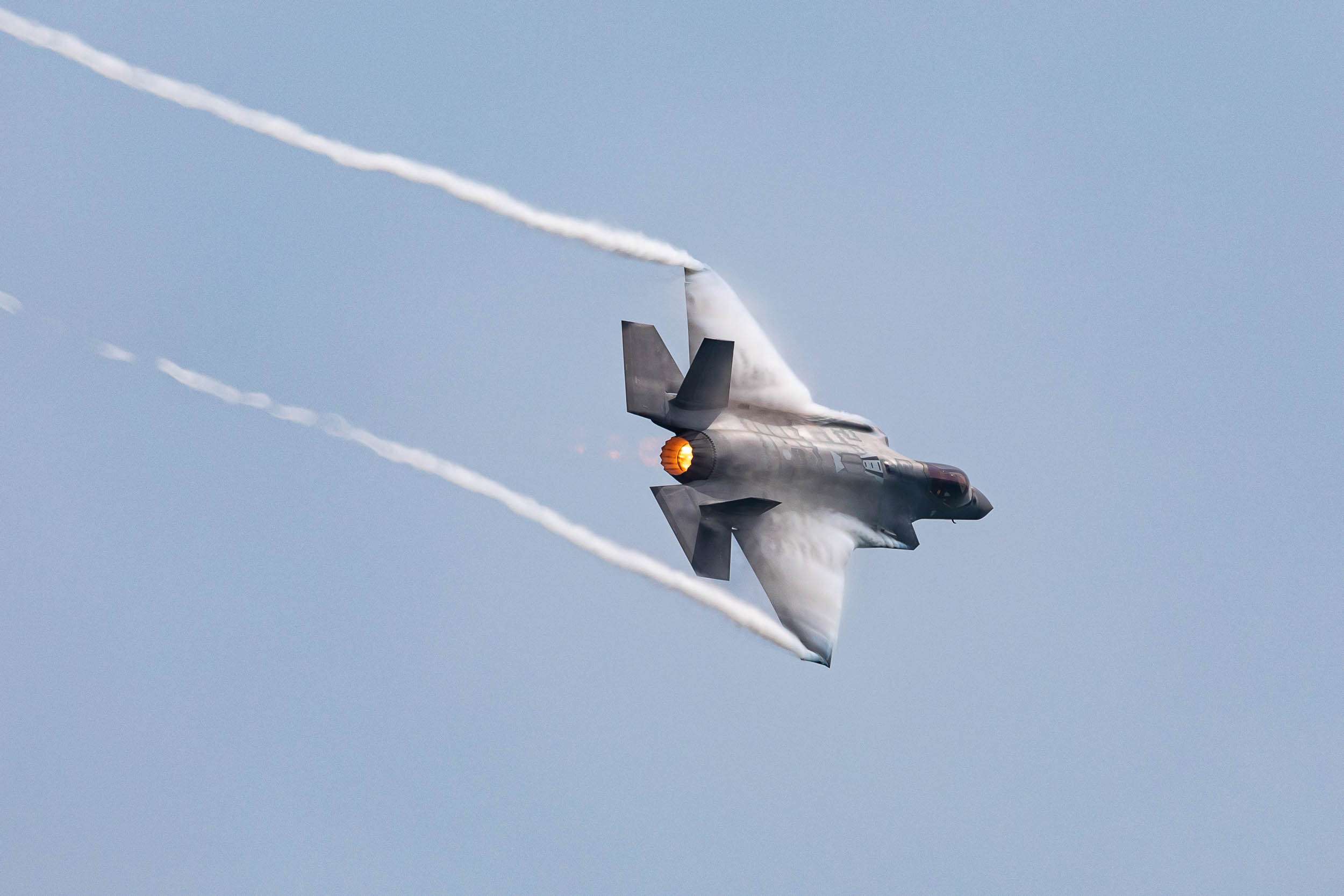 A US Air Force F-35 flies at high speed with visible vapor and afterburner