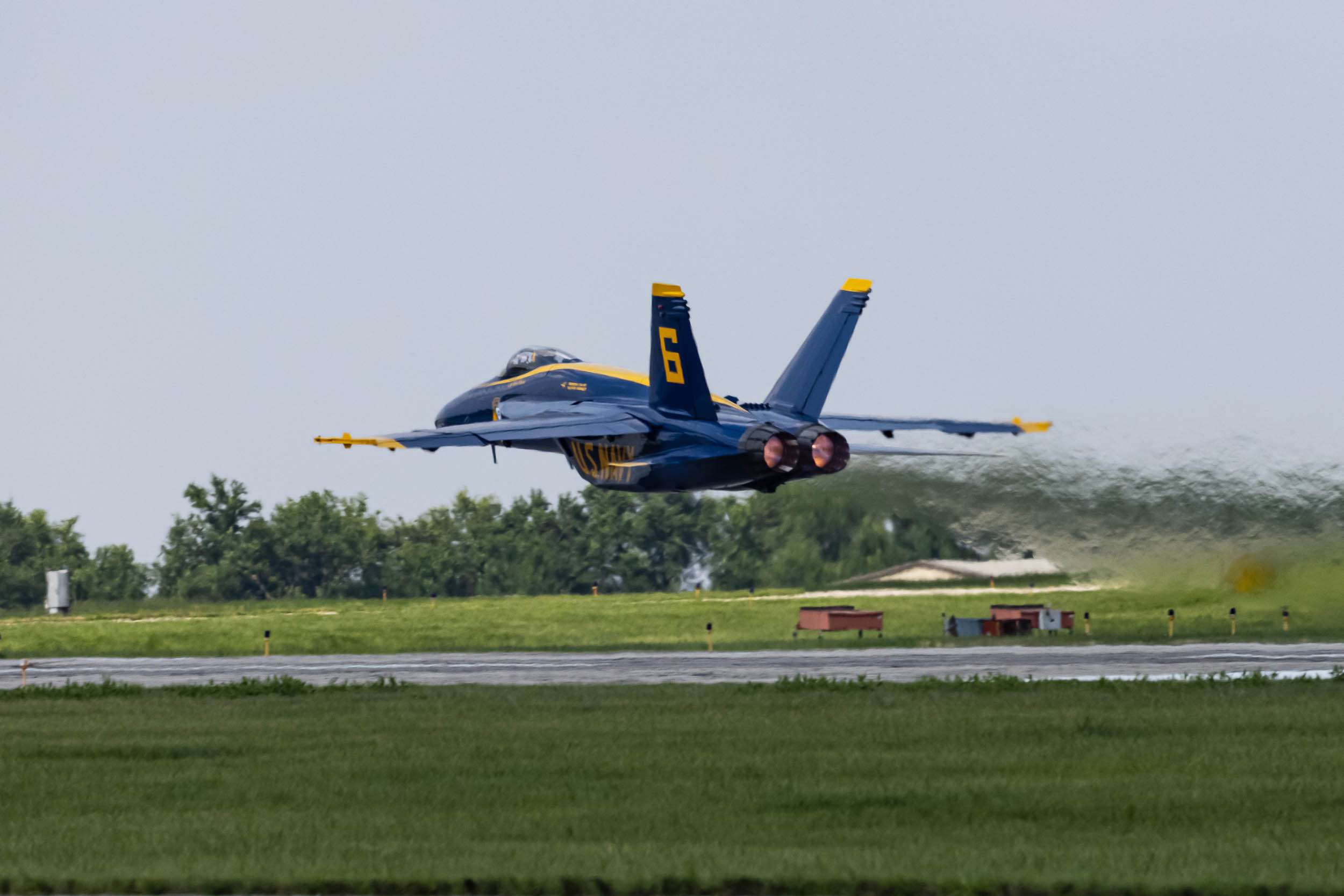 A US Navy Blue Angels jet flies only a few feet above the runway with full afterburner